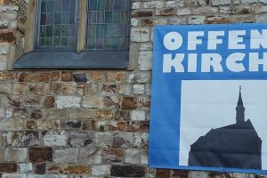 An einer Hauswand hängt ein Plakat mit den Worten: Offene Kirche.