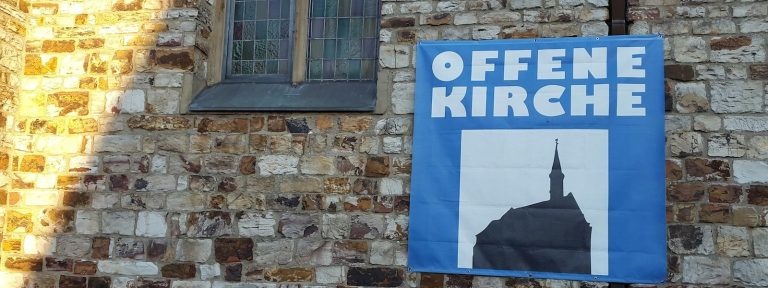 An einer Hauswand hängt ein Plakat mit den Worten: Offene Kirche.