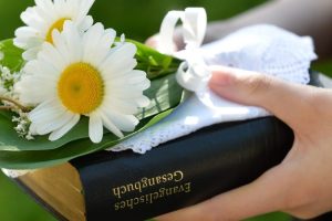 Konfirmandin mit Gesangbuch und Blumen.